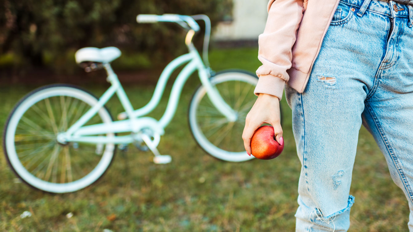 Girl holding an apple with bike in the background